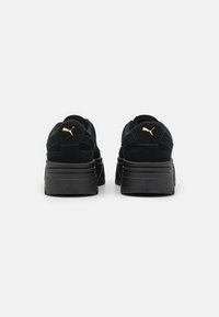 Baskets en daim noir avec une semelle noire épaisse. Elles présentent un détail de logo doré sur le talon, une texture lisse et un col rembourré au niveau de la cheville.