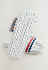Sandale albe cu talpă în formă de slide, cu un accent dungat în roșu, alb și albastru pe bretea. Au o talpă texturată pentru aderență și o talpă moale și netedă pentru confort.