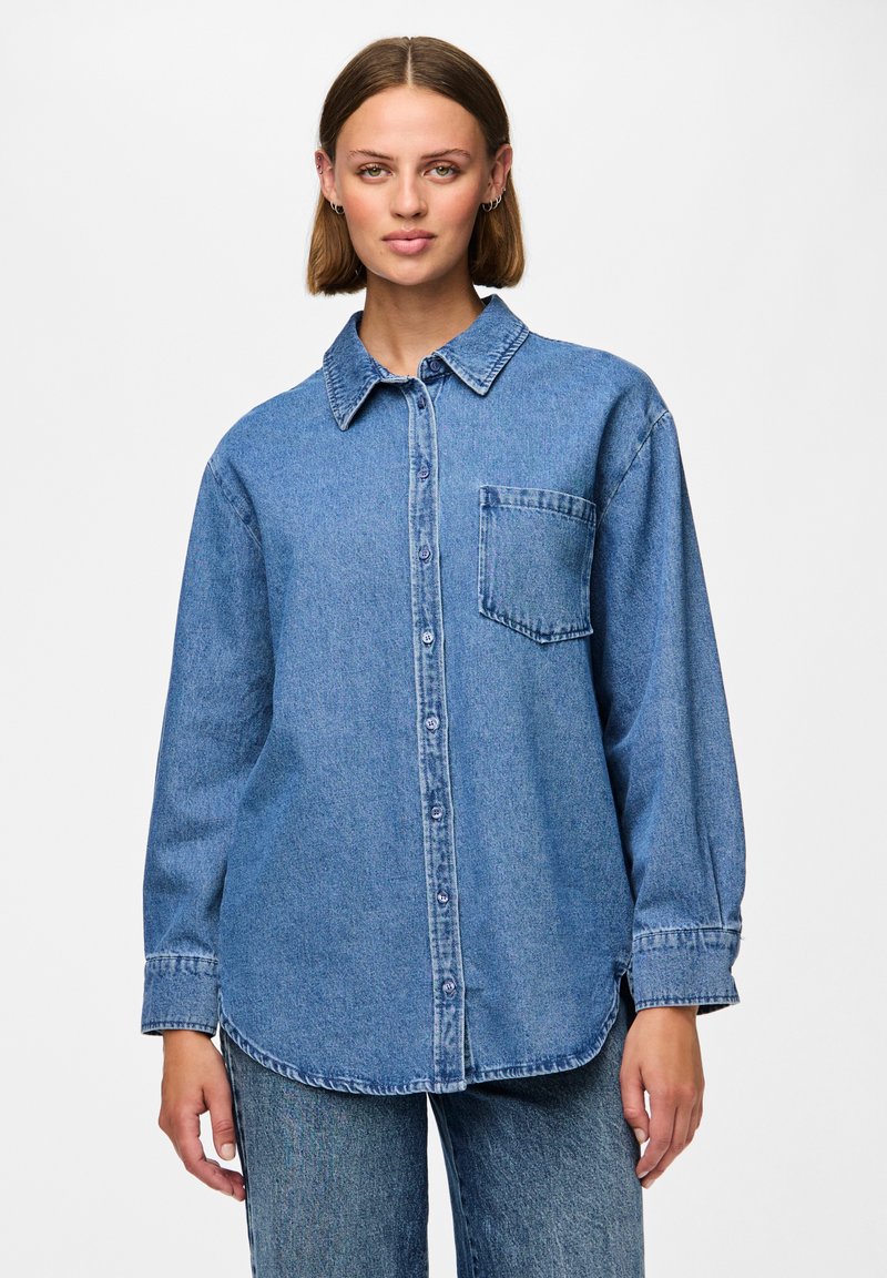 Modra denim srajca s gumbi in dolgimi rokavi, z ostrim ovratnikom in žepom na prsih. Tkanina ima mehak, rahlo teksturiran videz.