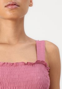 Rosa gesmocktes Oberteil mit breiten Trägern und Rüschendetails, strukturiertem Stoff und taillierter Passform, die ein weiches, lässiges Erscheinungsbild verleiht.