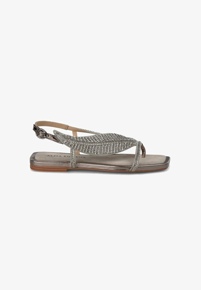 Sandal flat in argento metallico con un design impreziosito da strass. Caratterizzata da punta aperta e cinturino posteriore regolabile. Soletta liscia e opaca.