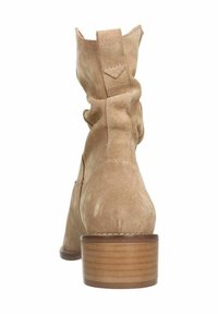 Stivaletto in suede beige con design morbido, punta arrotondata e tacco in legno impilato. La vista posteriore mostra le cuciture e la parte superiore affusolata.