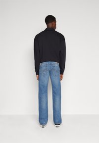 Polo à manches longues noir associ�é à un jean large bleu clair. Les détails notables incluent des coutures contrastantes sur les poches et un design simple.