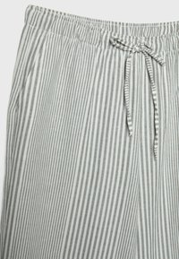 Pantalon rayé vertical gris et blanc avec une ceinture élastique et un cordon noué à l'avant, doté de poches latérales.
