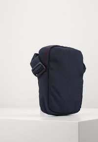 Borsetta in tessuto blu marine dalla forma rettangolare, con cuciture rosse e una tracolla regolabile. Texture liscia, design compatto per portare l'essenziale.