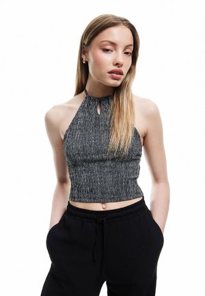 Top corto a halter a righe bianche e nere con apertura a chiave sul colletto, realizzato in un tessuto texture. Abbinato a pantaloni neri.