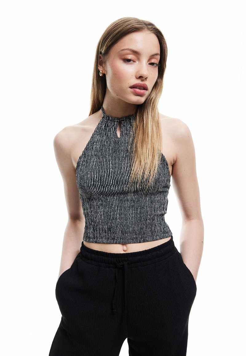 Czarna i biała w paski halterka typu crop top z wycięciem w dekolcie, wykonana z teksturowanej tkaniny. Połączona z czarnymi spodniami.