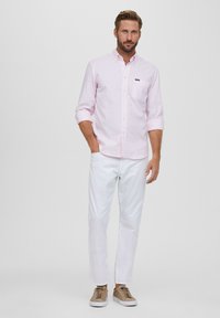 Lichtroze, lange mouwen blouse met knopen en een borstzak, gecombineerd met witte broeken en tan sneakers, wat een casual uitstraling geeft.