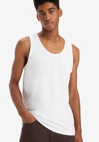 Top in cotone bianco senza maniche con scollatura a U e vestibilità rilassata. Caratterizzato da una superficie liscia e un design minimalista, ideale per essere indossato a strati.