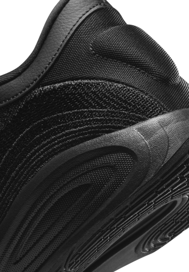 Zapato deportivo negro con parte superior de malla texturizada y elegantes acentos de cuero. La suela exterior tiene un diseño estampado para proporcionar agarre y flexibilidad.