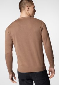 Brązowy sweter robiony na drutach z długimi rękawami, prążkowanymi mankietami i dołem. Posiada okrągły dekolt i gładką teksturę, ukazany z widoku z tyłu.