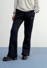 Fekete, laza szabású sportnadrág, zsinóros derékkal, puha anyagból készült, a bal combján egy kis fehér Nike logóval.