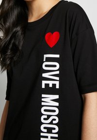 Svart bomullströja med en röd hjärtgrafik på bröstet och frasen "LOVE MOSCHINO" i fetvita bokstäver längs sidan.