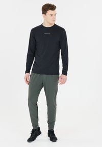 Svart långärmad träningsskjorta med texten "ENDURANCE", parat med gröna träningsbyxor med svarta sidodetaljer och svarta sneakers.