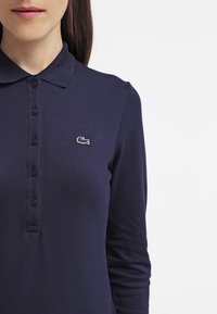 Polo à manches longues en tissu texturé bleu marine, doté d'une patte de boutonnage à trois boutons et d'un logo brodé sur la poitrine gauche.