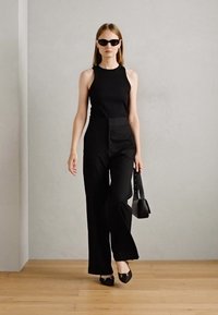 Top negro sin mangas combinado con pantalones negros de cintura alta. Los accesorios incluyen gafas de sol negras y un pequeño bolso negro.