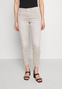 Ljust beige jeans med slim fit, fem fickor och dragkedja. I kombination med svarta klacksandaler. Slät denimtextur.