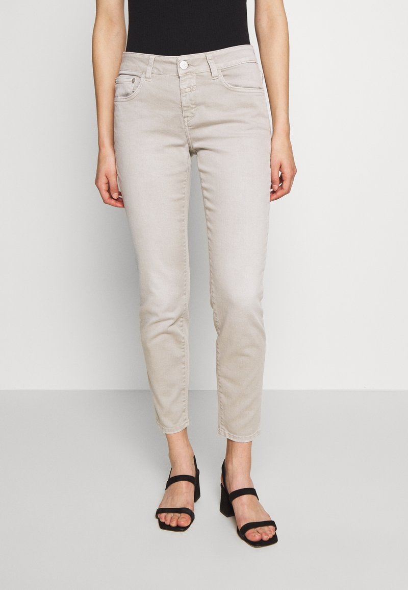 Ljust beige jeans med slim fit, fem fickor och dragkedja. I kombination med svarta klacksandaler. Slät denimtextur.