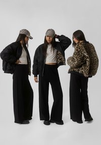 Crna bomber jakna s podstavljanjem u leopard printu, uparena s kapom u leopard printu i širokim crnim hlačama, s mekanom teksturom i slobodnim krojem.