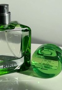 Grønn glassparfymeflaske med rektangulær form og sølv spraydyse, ledsaget av en rundet grønn glassdekorasjon.