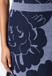 Rochie tricotată cu un model floral în nuanțe de bleumarin și albastru deschis, având o talie elastică cu model în triunghiuri. Țesătura are o textură fină și un luciu subtil.