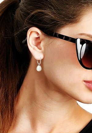 Boucles d'oreilles en argent avec un pendentif en perle blanche, présentant une finition polie et un design lisse et arrondi, mis en valeur par une fine créole.