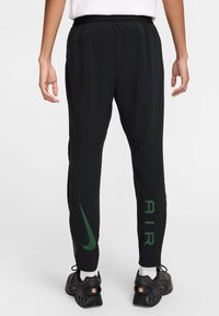 Pantalons de sport noirs à coupe slim, arborant un logo Nike vert et le texte "AIR" sur la jambe gauche. Fabriqués en matériau léger et flexible.