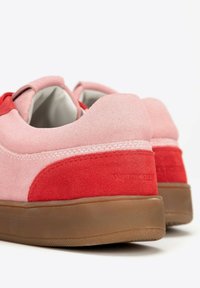 Sneakers in suede rosa con accenti rossi e soletta in gomma marrone. Presentano una texture liscia e una forma arrotondata con dettagli cuciti.