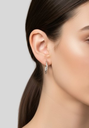 Boucle d'oreille en argent tordu affichée sur l'oreille d'un modèle, mettant en valeur une forme circulaire avec une surface texturée.