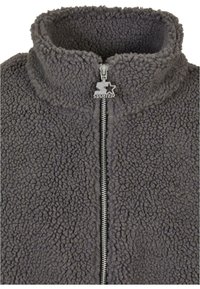 Grå fleece zip-up jakke med høj krave og sølvfarvet lynlås. Tekstureret overflade med en blød, luksuriøs følelse. Brandlogo vedhæftet.