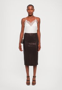 White camisole with lace trim paired with a fitted, dark sequin pencil skirt. Model wears strappy black heels and holds a small purse.