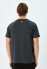 T-shirt corto grigio scuro con colletto girocollo e maniche raglan. Presenta un logo geometrico sottile sulla parte superiore della schiena. Tessuto morbido.