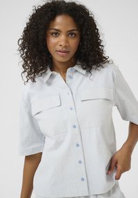 Camicia a maniche corte a strisce blu e bianche con colletto, due taschini sul petto e bottoni azzurri. Tessuto morbido con una vestibilità rilassata.