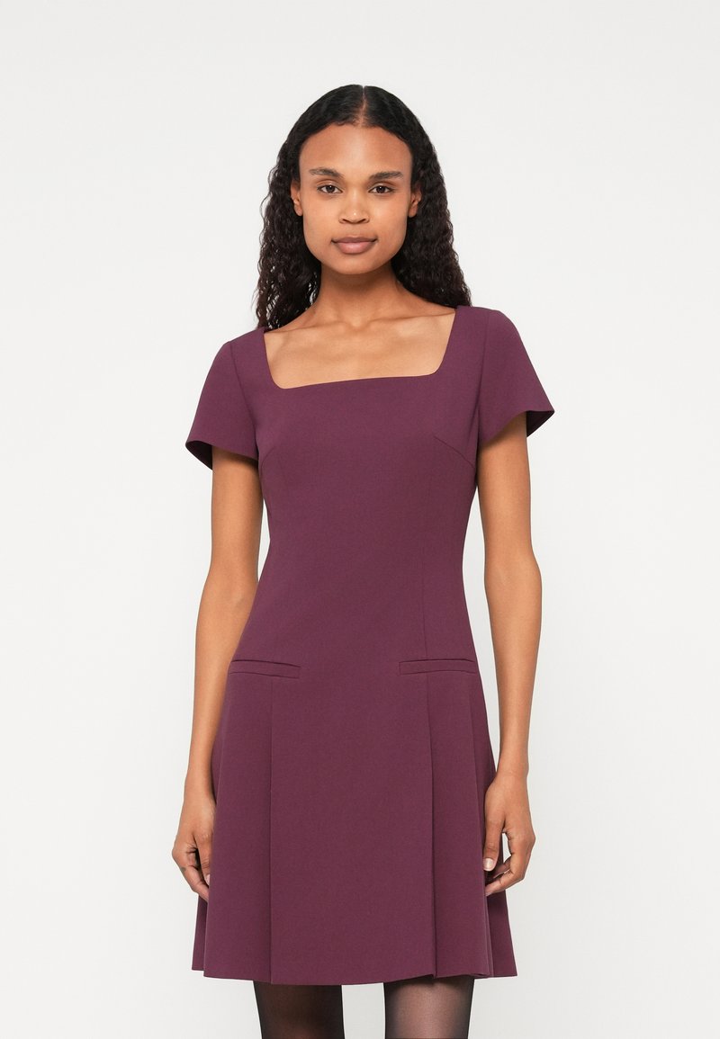 Rochie bordeaux cu mâneci scurte, decolteu pătrat și două buzunare în față. Fustă evazată și textură netedă. Design minimalist.