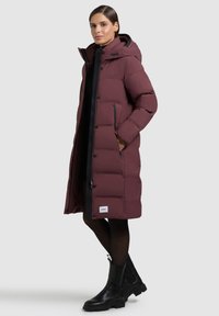 Burgundipunane kapuutsiga turske talvejope, vertikaalse tikandimustriga, mustade detailidega, ees tõmblukuga ja küljetaskutega. Kandmisel mustad pahkluud saabastel.