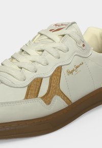 Baskets blanc crème avec détails latéraux texturés marron clair, lacets blancs, semelle marron et petit logo "Pepe Jeans London" sur le côté.