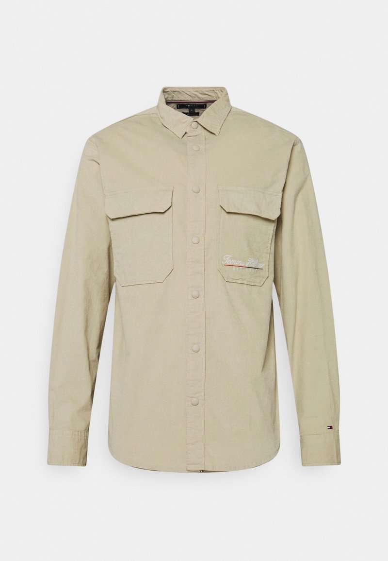 Camicia button-up beige con maniche lunghe, due grandi tasche frontali e ricamo "Tommy Hilfiger" sulla tasca destra.