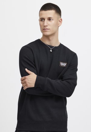 Zwarte sweatshirt met een ronde halslijn, ribgebreide manchetten en zoom, met een klein rechthoekig logo-opdruk op de borst. Glad textuur.