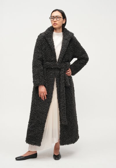 Dugi, tamnosivi, pahuljasti kaput s širokim ovratnikom i remenom. Tekstura je mekana, s hrapavim dizajnom. Nošen preko bijele haljine.