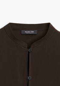 Brązowa koszula z guzikami, z okrągłym kołnierzykiem, dwoma czarnymi guzikami i delikatnymi szwami wzdłuż dekoltu. Metka głosi "Massimo Dutti."