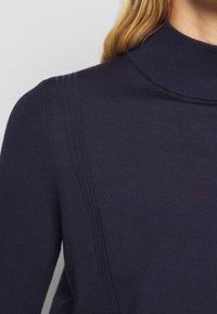 Granatowy sweter z golfem o prążkowanej strukturze, charakteryzujący się dopasowanym krojem oraz teksturowanym materiałem z subtelnymi, pionowymi szwami.