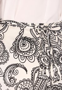 Sorte og hvide mønstrede stof med spiraler og blomsterdesigns, med en bundet taljedetail og glat tekstur.