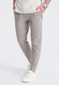 Joggers grises de tejido suave, con un ajuste slim, bolsillos laterales y detalles de panel en contraste. Combinados con zapatillas blancas de tiras.