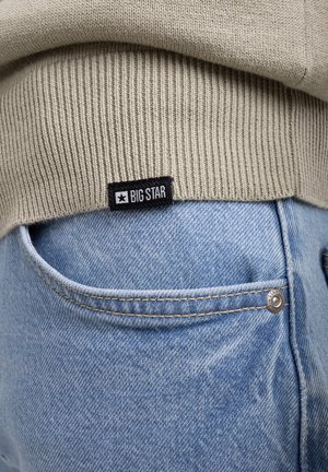 Súeter de punto gris claro con puños acanalados, etiquetado "BIG STAR", sobre jeans de mezclilla azul desgastado con un bolsillo visible y detalle de botón de metal.