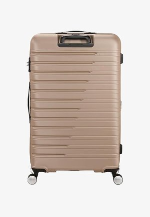 Valigia rigida grande beige con scanalature orizzontali, quattro ruote girevoli e maniglia nera per il trasporto sulla parte superiore e sul lato.