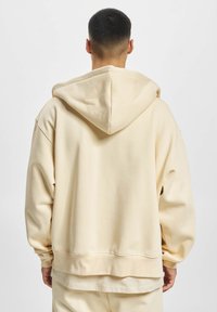 Beige oversized hoodie med snoretræk i hætten, lange ærmer og ribkant. Lavet af blødt, glat stof med et afslappet pasform-design.