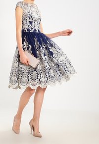 Marinblå klänning i spets med silverbroderi, korta ärmar och utställd kjol. Matchad med en ljuskuvertväska och nakna klackar.