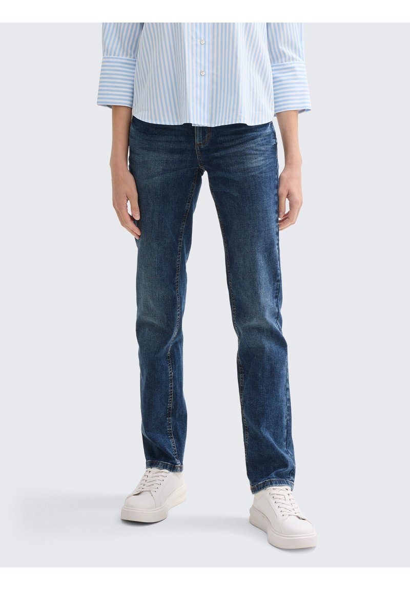 Jean bleu foncé à coupe droite avec un délavage subtil, associé à une chemise rayée bleu clair et des baskets blanches.