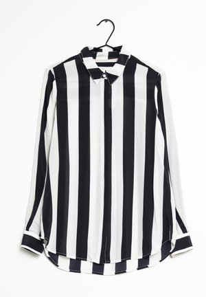 Camicia a maniche lunghe a righe bianche e nere con colletto, chiusura a bottoni e orlo arrotondato. Il tessuto sembra leggero e liscio.