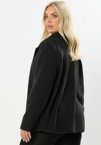 Svart fleecejacka med skräddarsydd design, med en skarp krage, långa ärmar och en mjuk textur. Tydliga sömmar och rena linjer.